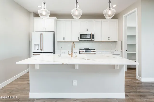 a kitchen with stainless steel appliances a sink a stove a refrigerator and white cabinets