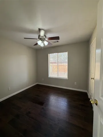 an empty room with wooden floor chandelier fan and windows