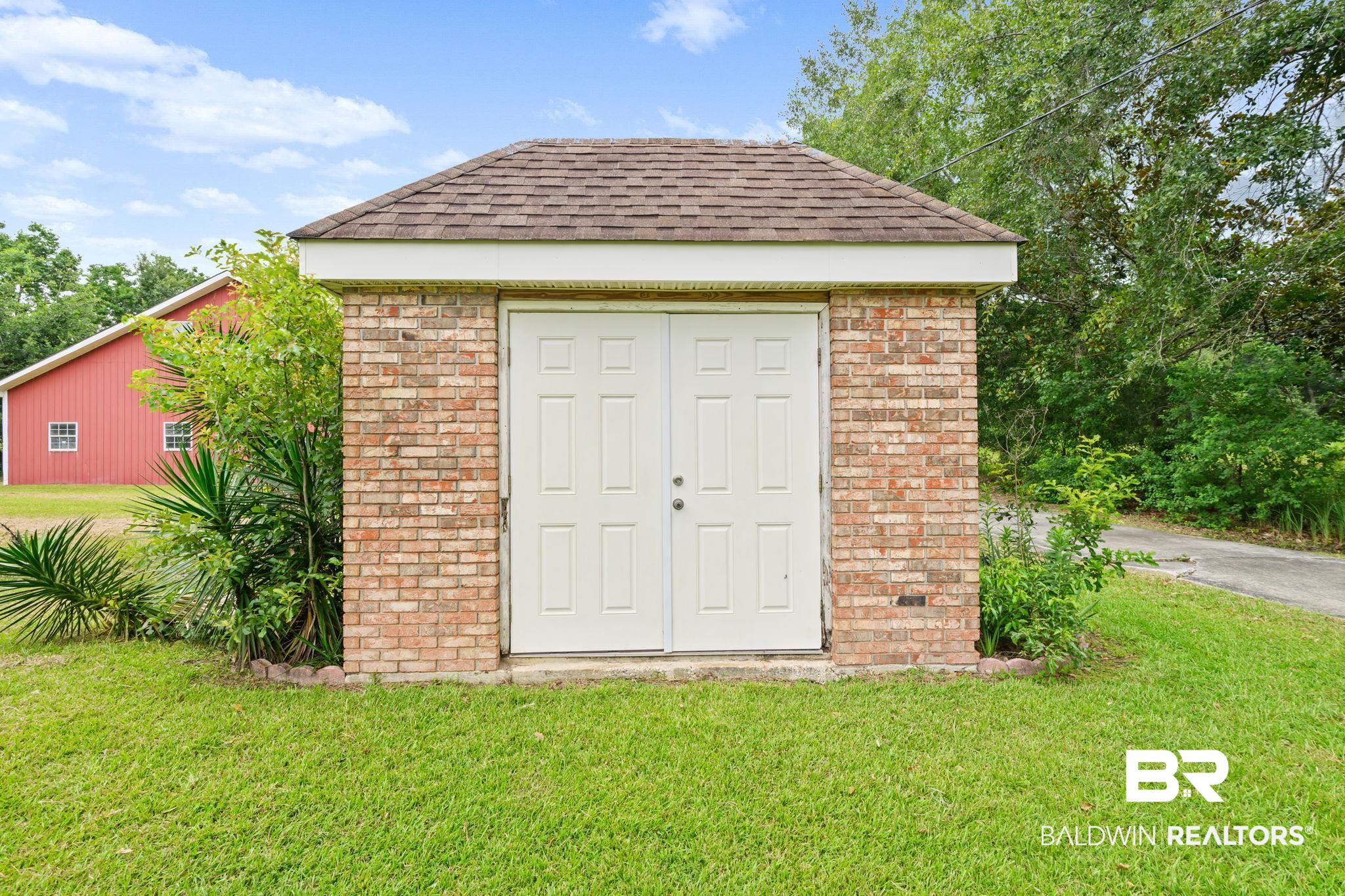 7540 2 Mile Road Irvington, AL 36544 - Photo 69 of 82 Brick exterior storage shed with dual white panel doors, a shingled roof, and white trim
