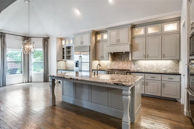 a kitchen with stainless steel appliances granite countertop a stove a sink and white cabinets with wooden floor