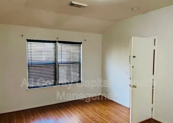 a view of an empty room with wooden floor and a window