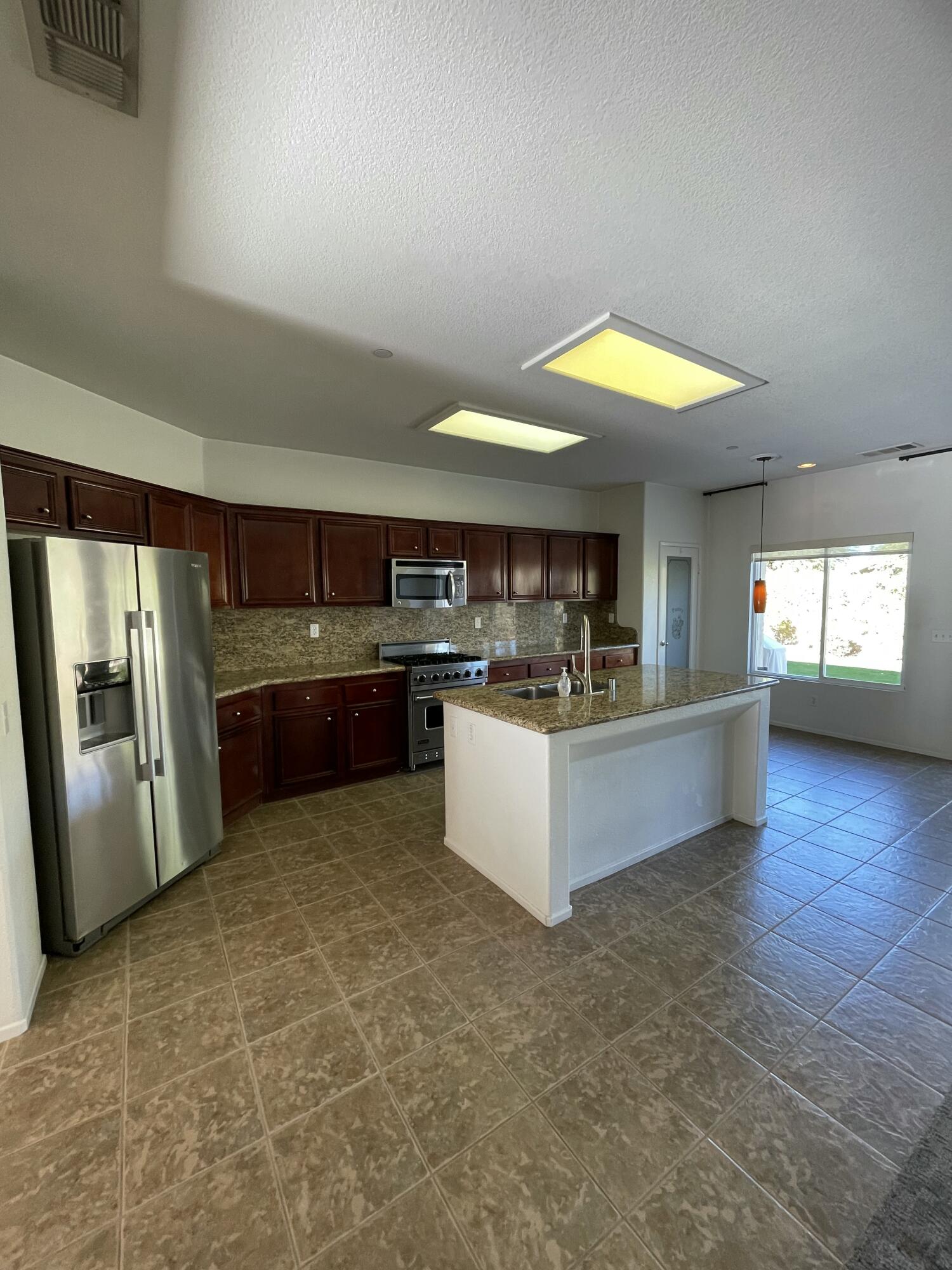1122 Oro Ridge Palm Springs, CA 92262 - Photo 26 of 33 a large kitchen with stainless steel appliances granite countertop a refrigerator a sink dishwasher a stove and a dining table with wooden floor