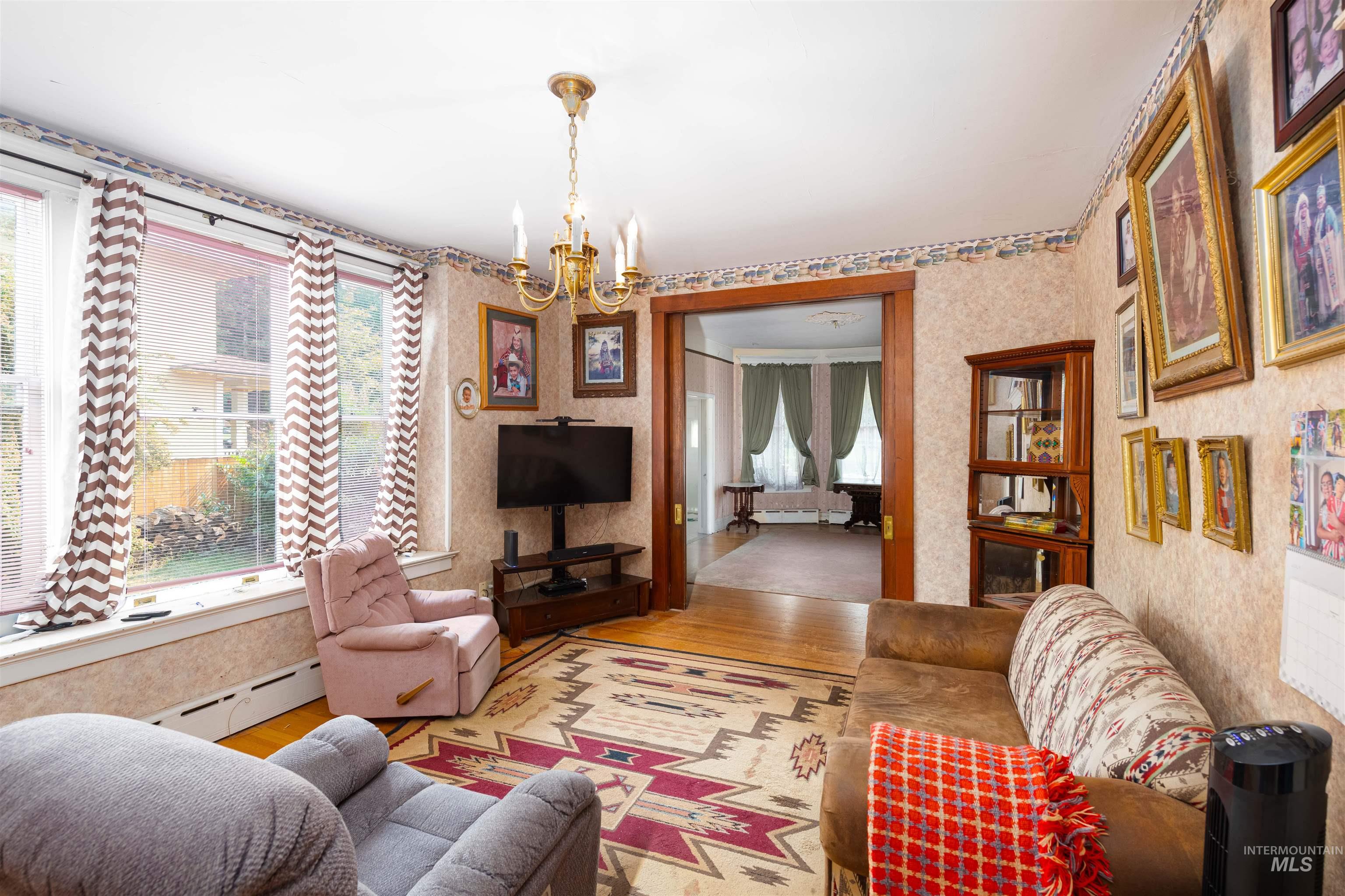 507 7th Avenue Lewiston, ID 83501 - Photo 10 of 30 Living room featuring wood finished floors, a chandelier, baseboard heating, and wallpapered walls