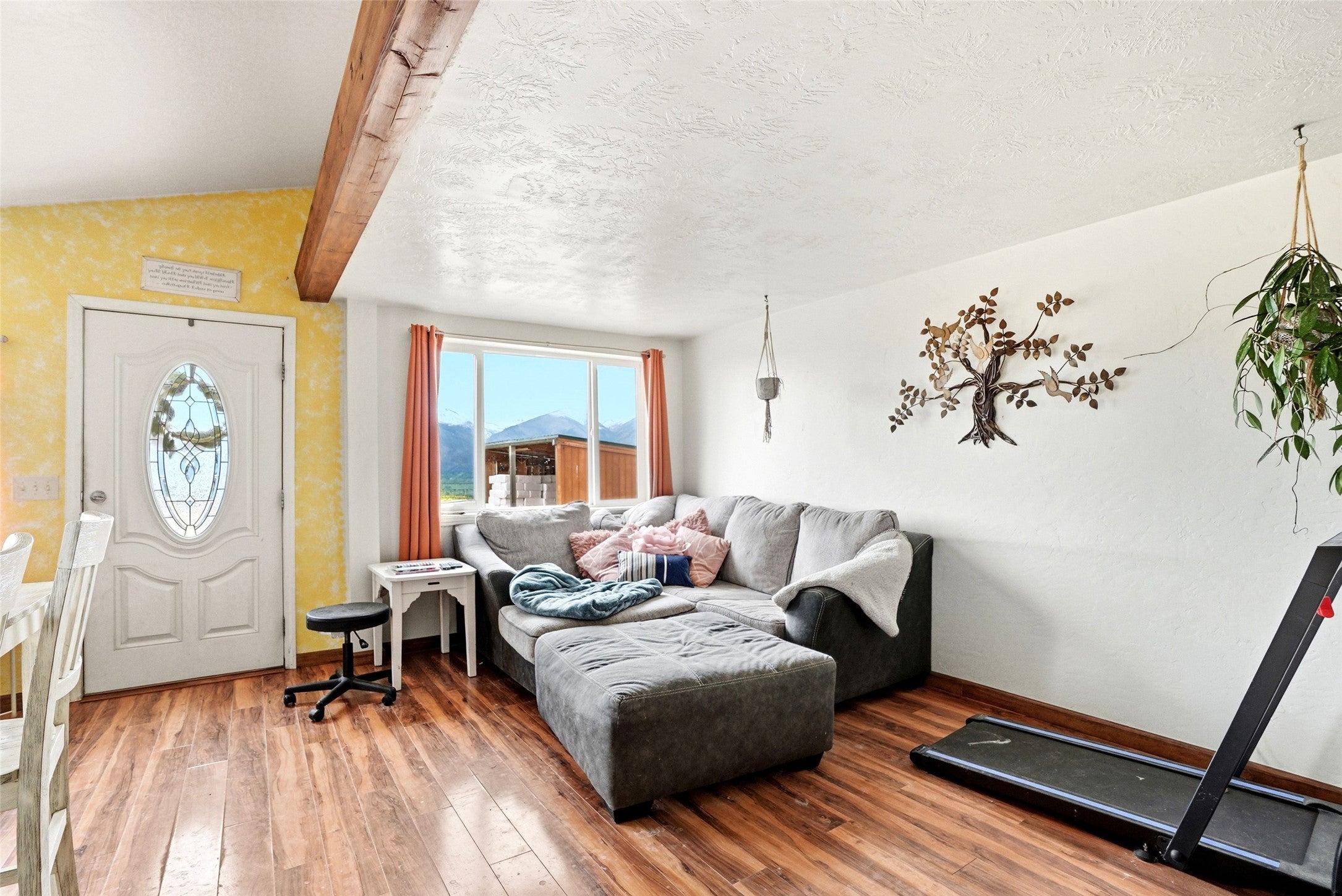 679 Hidden Valley Road North Florence, MT 59833 - Photo 62 of 85 Living area featuring wood-finish flooring, a white entry door with an oval leaded glass insert, a large window, and an exposed wood beam