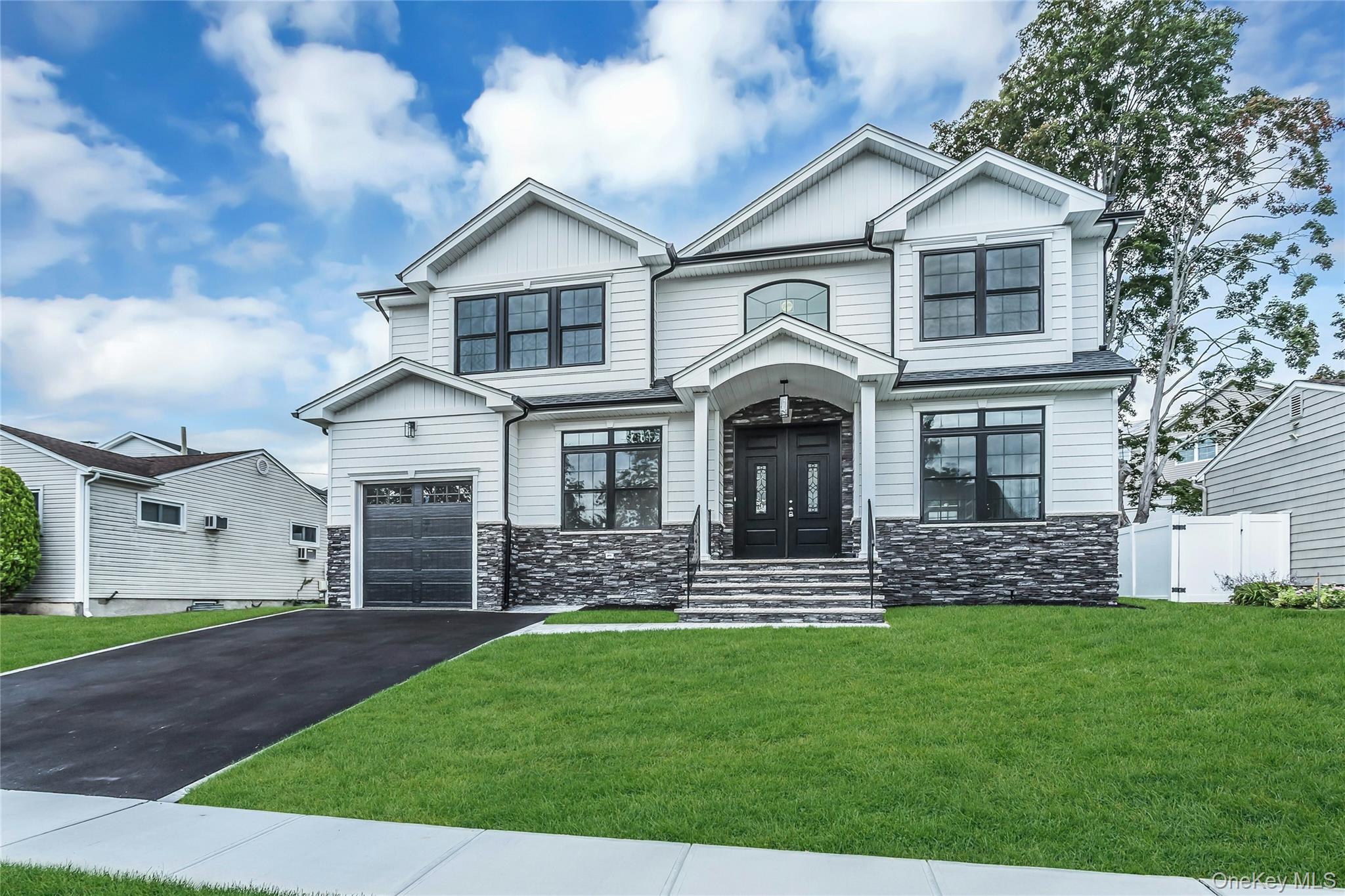 View of front of property with stone siding, a front lawn, asphalt driveway, board and batten siding, and an attached garage