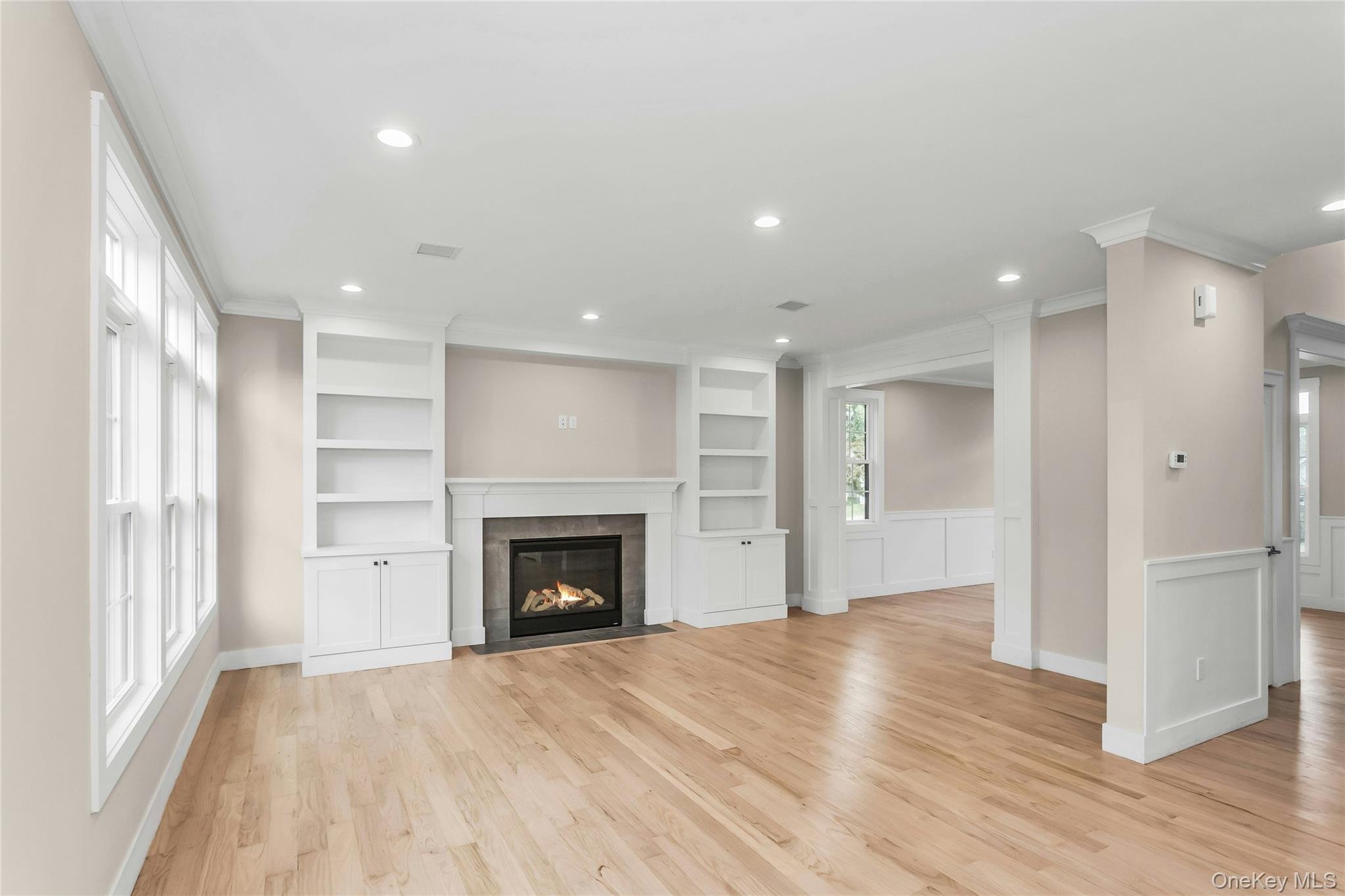 8 Sebree Place Plainview, NY 11803 - Photo 11 of 26 Unfurnished living room featuring recessed lighting, light wood-type flooring, a fireplace with flush hearth, ornamental molding, and built in shelves