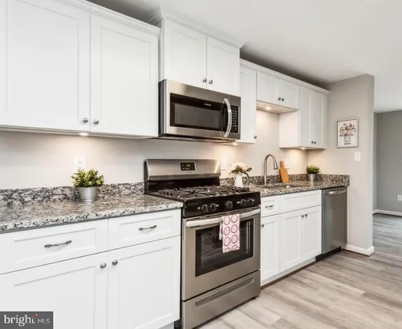 a kitchen with stainless steel appliances granite countertop grey cabinets a stove a sink and a microwave