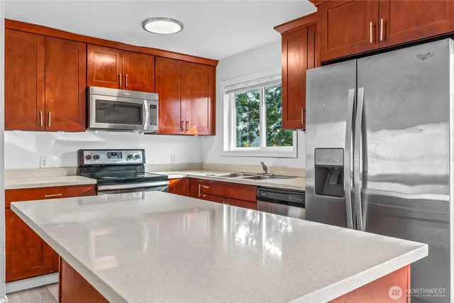 a kitchen with stainless steel appliances granite countertop a refrigerator a stove and a sink with wooden cabinets