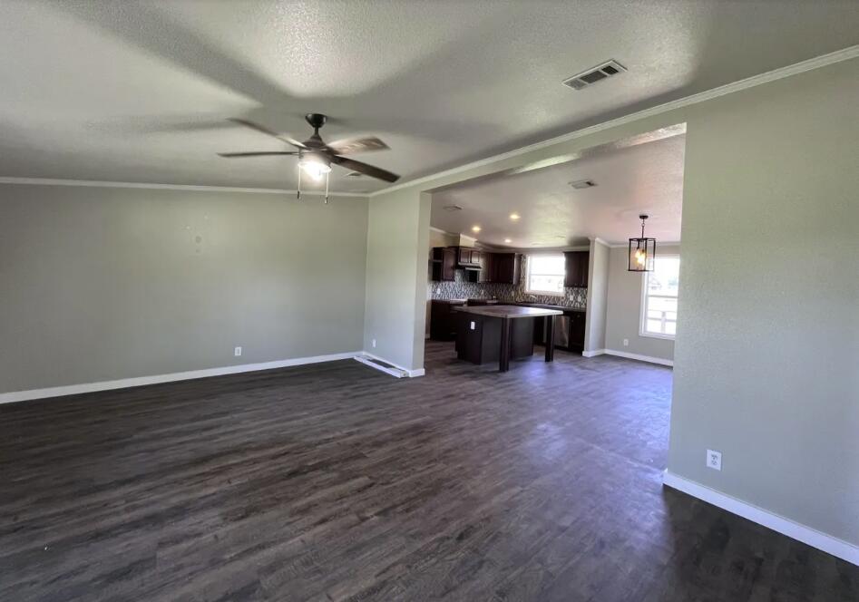 107 Grant Street Smyer, TX 79367 - Photo 8 of 22 an empty room with wooden floor ceiling fan and kitchen view