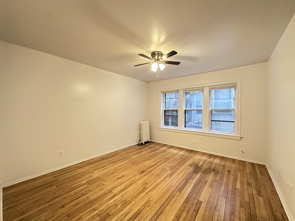 7149 South Constance Avenue, Unit 1E Chicago, IL 60649 - Photo 12 of 20 a view of an empty room with a window and wooden floor
