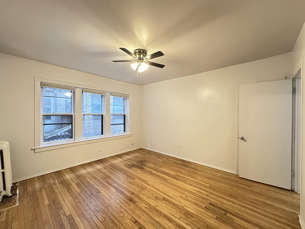 7149 South Constance Avenue, Unit 1E Chicago, IL 60649 - Photo 14 of 20 a view of an empty room with a window and wooden floor