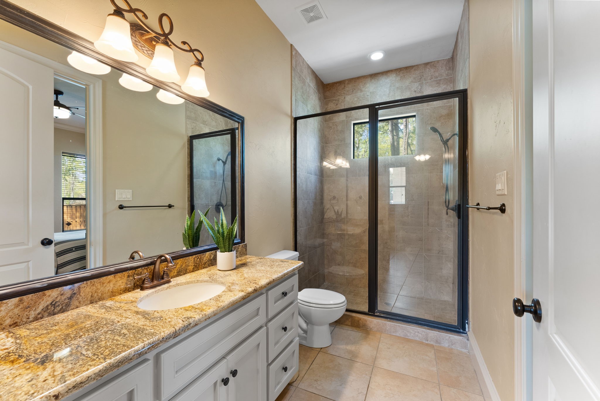 3907 Rayford Road Spring, TX 77386 - Photo 21 of 38 Designed with accessibility in mind, the downstairs en-suite bath (accessed fro the bedroom or utility) offers extra-wide doorways, a spacious granite vanity with ample storage, a framed mirror, and a walk-in shower with an upper transom window for natural light.