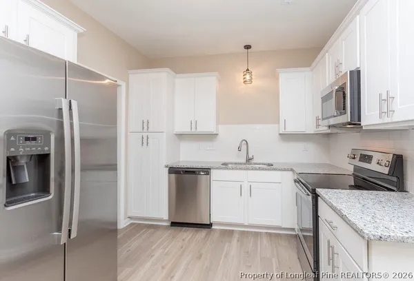 a kitchen with stainless steel appliances granite countertop a refrigerator a sink a stove and white cabinets with wooden floor