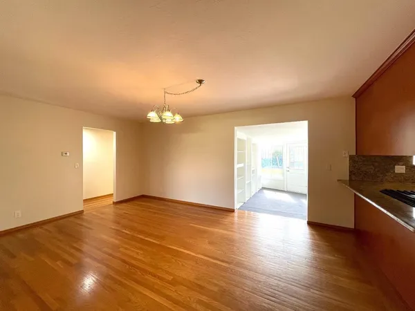 an empty room with wooden floor and kitchen view