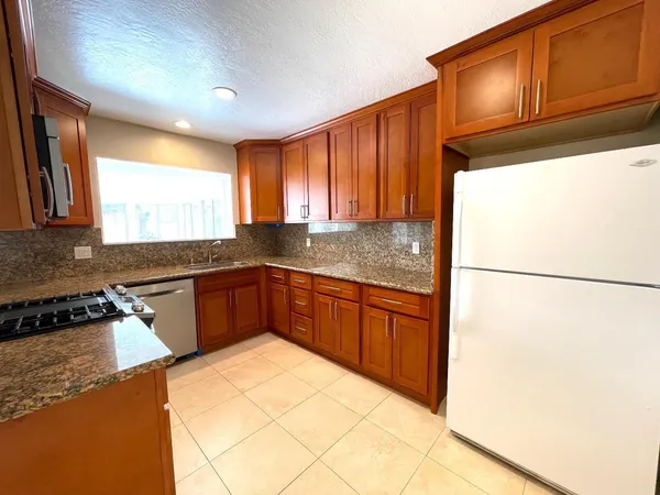 a kitchen with granite countertop a refrigerator a sink a stove a microwave and wooden cabinets