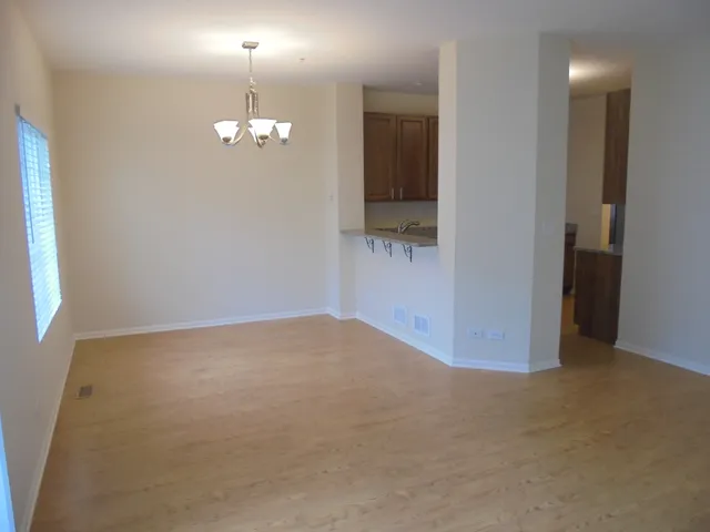 an empty room with chandelier fan and kitchen view