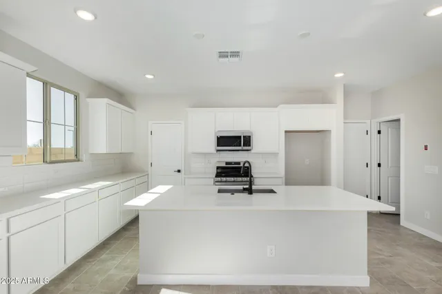 a large white kitchen with kitchen island a sink stainless steel appliances and cabinets