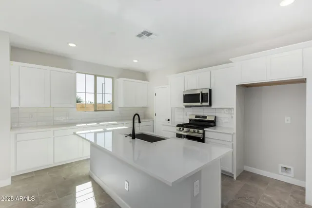 a kitchen with stainless steel appliances a sink a stove a microwave a center island and cabinets