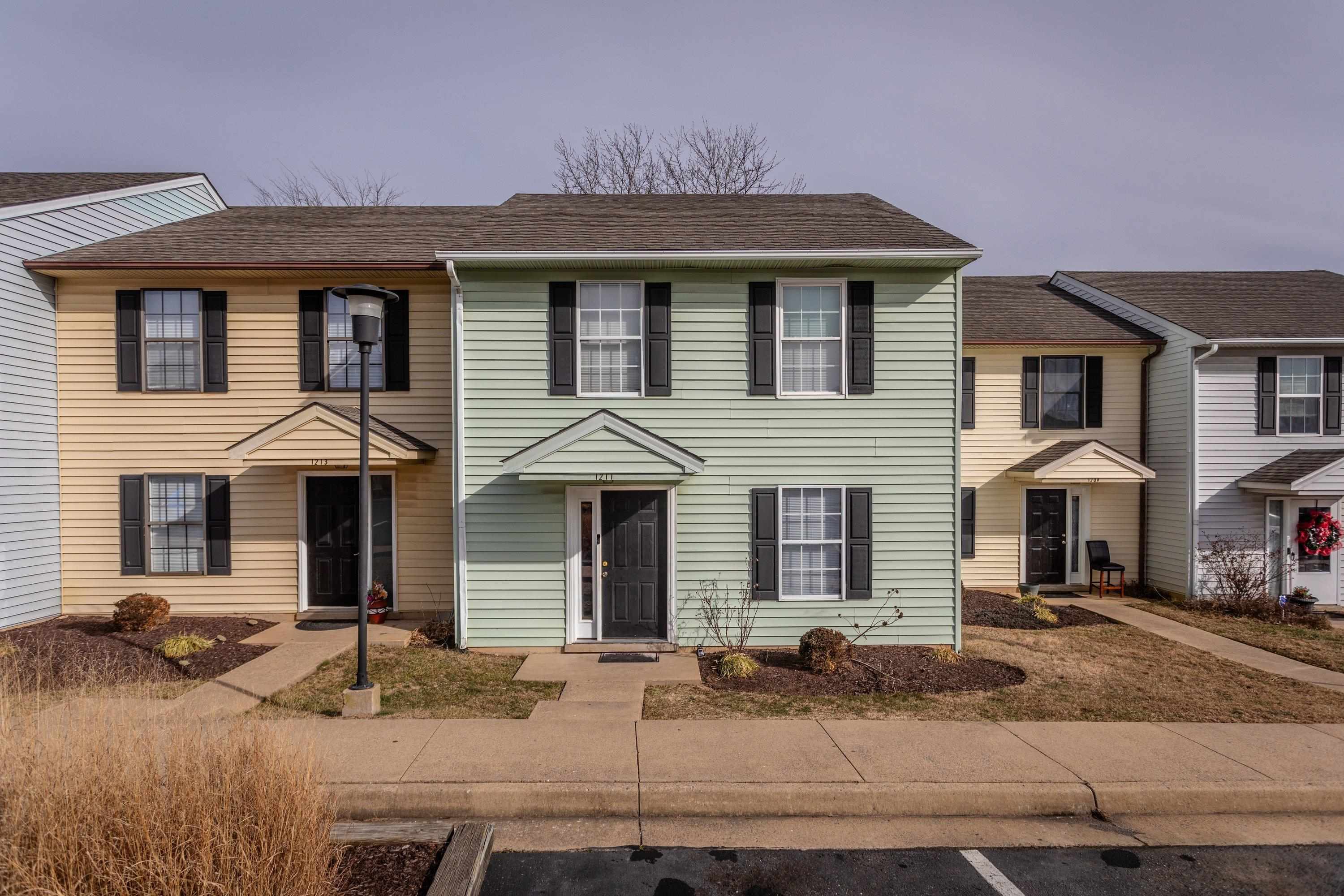 The front view of the townhouse highlights the sidewalks, multiple parking spaces, covered front porch space, and landscaping.