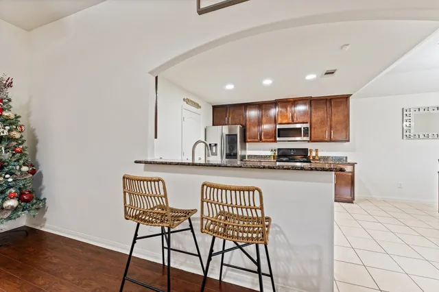 a kitchen with granite countertop kitchen island stainless steel appliances a refrigerator a stove a sink and a dining table with wooden floor