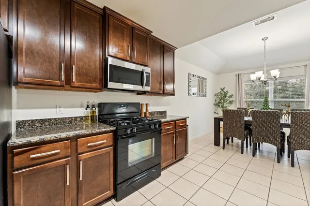 a kitchen with stainless steel appliances granite countertop a stove top oven a sink dishwasher a dining table and chairs with wooden floor