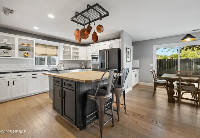 a kitchen with stainless steel appliances granite countertop a stove a sink dishwasher a dining table and chairs with wooden floor