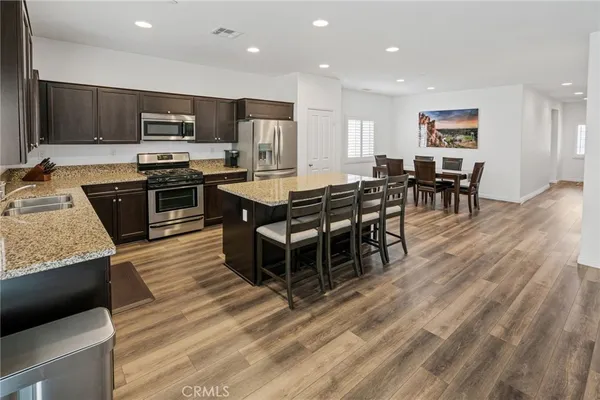 a kitchen with stainless steel appliances granite countertop a stove top oven a sink dishwasher a dining table and chairs with wooden floor