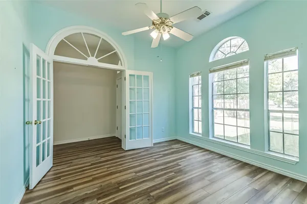 an empty room with wooden floor fan and windows