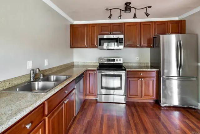 a kitchen with stainless steel appliances granite countertop a sink a stove a refrigerator cabinets and a wooden floor