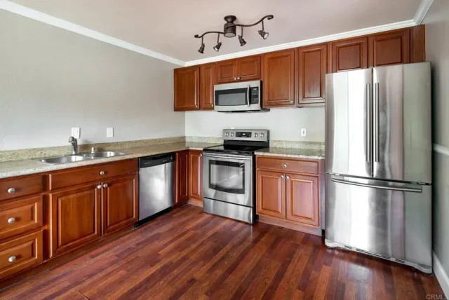 a kitchen with stainless steel appliances granite countertop a refrigerator a stove top oven a sink and dishwasher with wooden floor