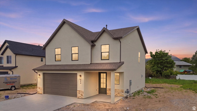 Contemporary two-story stucco exterior featuring a gabled roofline, stone veneer accents, an attached two-car garage with a brown door, and a covered entry