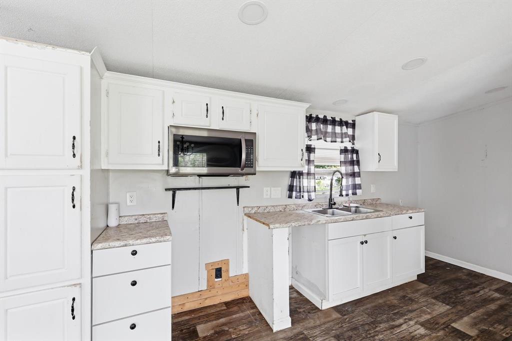 316 Summit Drive Springtown, TX 76082 - Photo 21 of 39 The kitchen features white cabinetry, a stainless steel microwave, a double basin sink with a dark faucet, and wood-look flooring