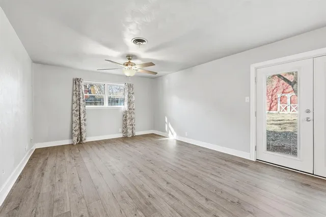 an empty room with wooden floor chandelier fan and windows