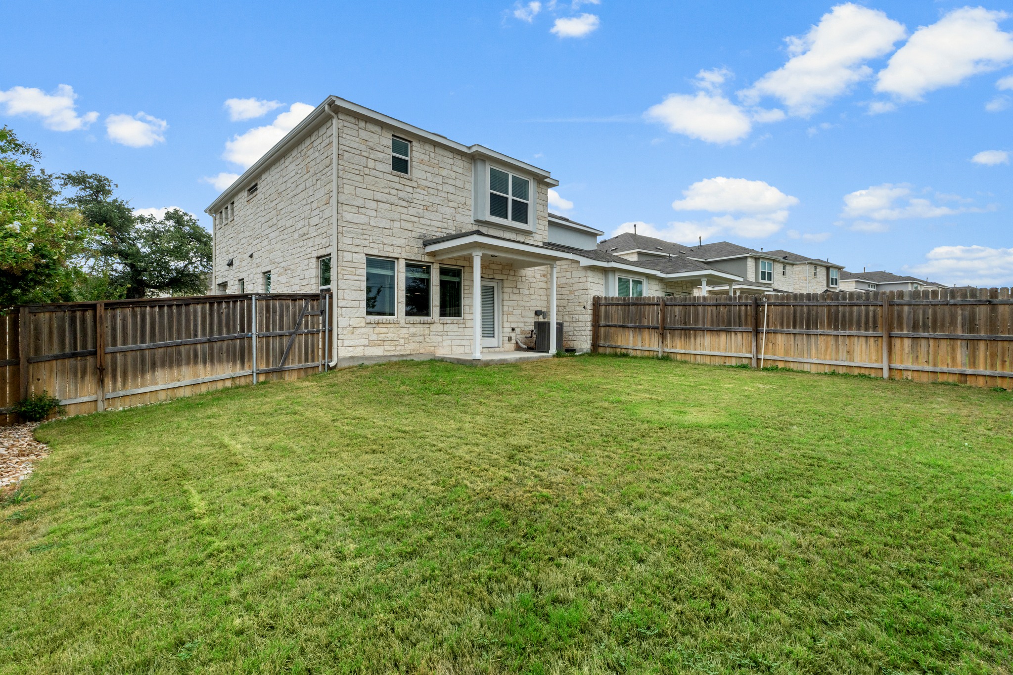 2251 Rocoso Trail Leander, TX 78641 - Photo 32 of 34 A spacious grassy lawn is fully enclosed by wooden fencing behind this two-story stone home.