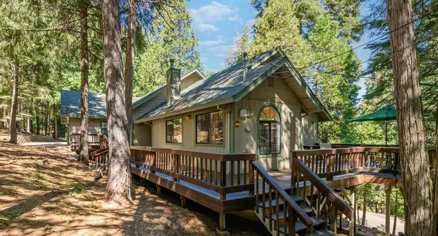 a view of a brick house with large trees and wooden fence