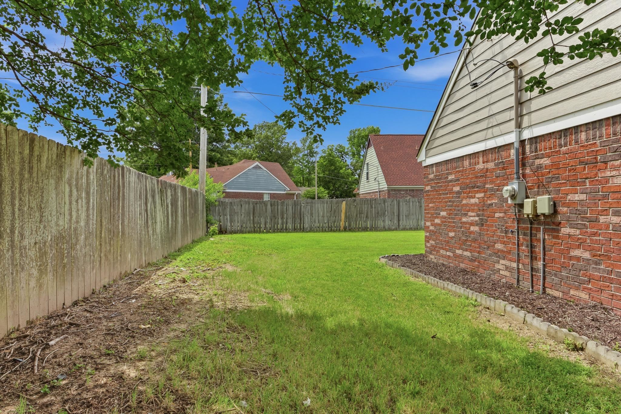 4101 Long Creek Road Memphis, TN 38125 - Photo 35 of 36 Expansive grassy yard area featuring a wooden privacy fence, brick exterior with beige siding, and mature tree canopy overhead