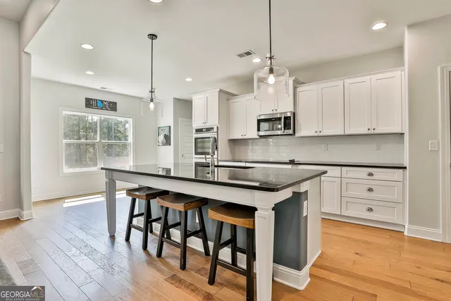 a kitchen with stainless steel appliances granite countertop a stove top oven a refrigerator a sink and white cabinets with wooden floor