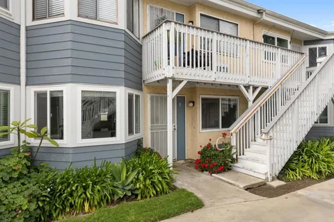 a view of a white house with large windows and flower plants