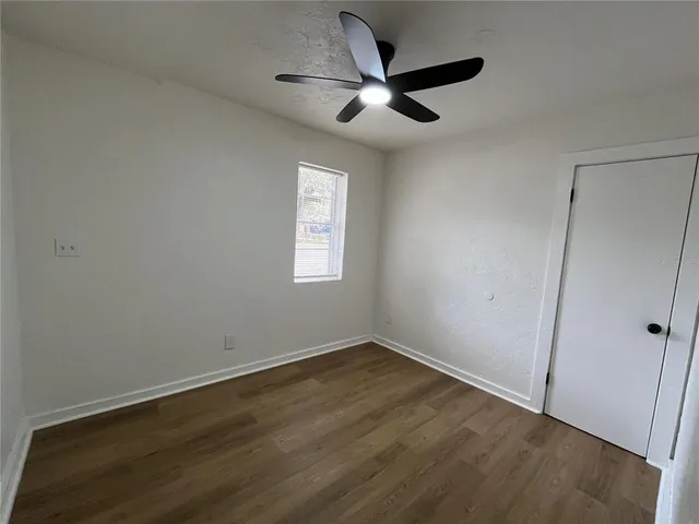 an empty room with wooden floor fan and windows