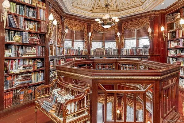 a view of a living room that has a chandelier and a bookshelf with wooden floor