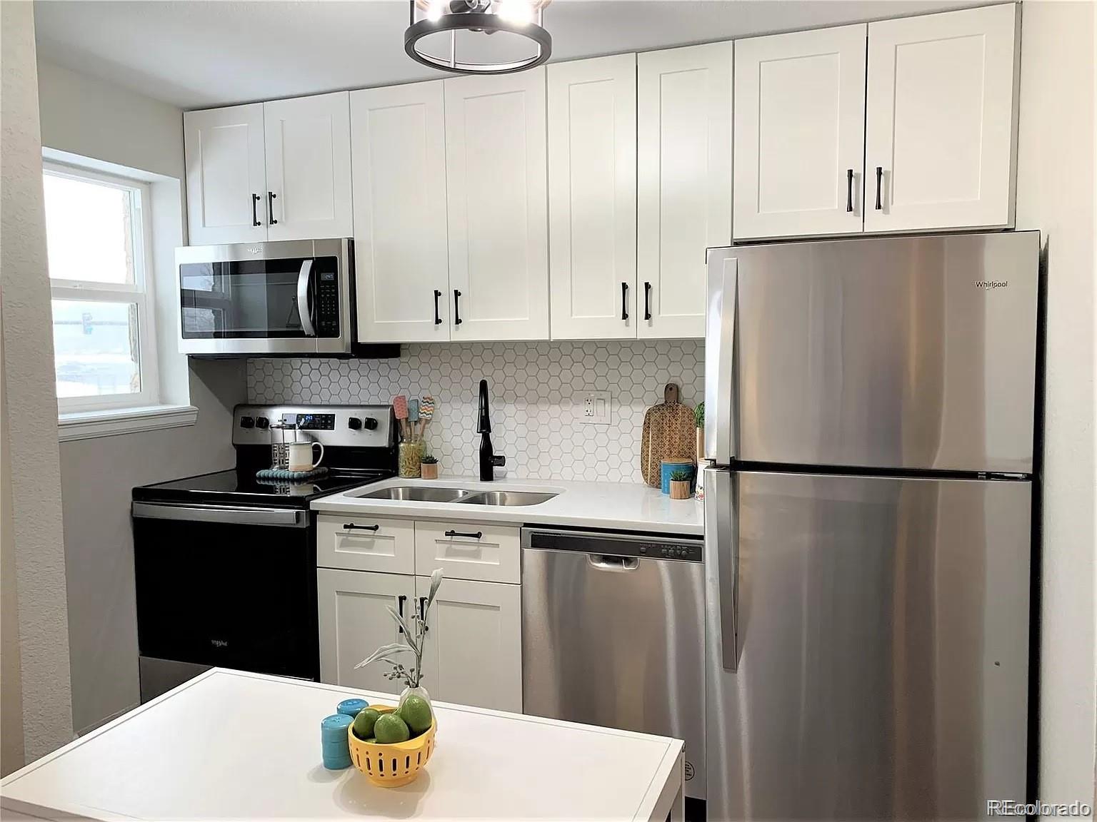 a white kitchen with stainless steel appliances granite countertop a refrigerator a stove a sink and a microwave