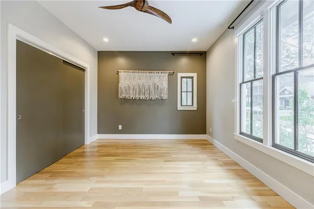 a view of an empty room with wooden floor and a ceiling fan