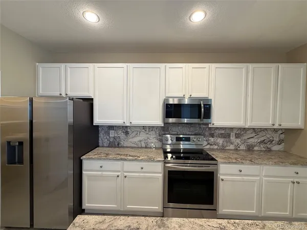 a kitchen with stainless steel appliances granite countertop a stove a refrigerator a sink and white cabinets