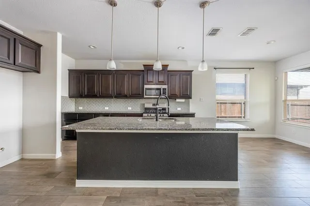 a kitchen with stainless steel appliances granite countertop a sink a stove and a wooden floor
