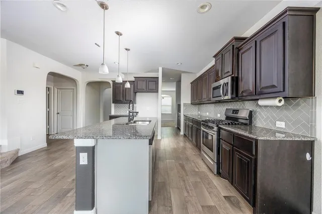 a kitchen with stainless steel appliances granite countertop a sink a stove and a wooden floors