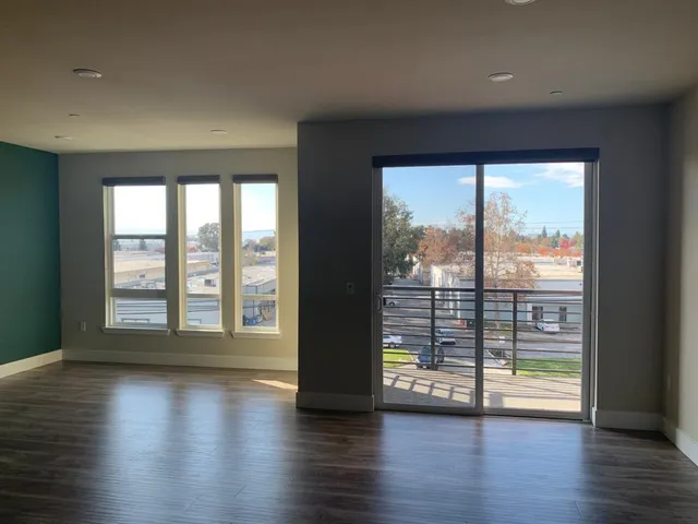 an empty room with wooden floor and windows with curtains