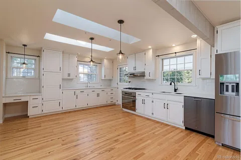 a kitchen with stainless steel appliances granite countertop a refrigerator a sink dishwasher a stove and white countertops with wooden floor