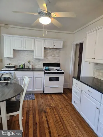 a kitchen with granite countertop a stove a sink dishwasher a refrigerator and white cabinets with wooden floor