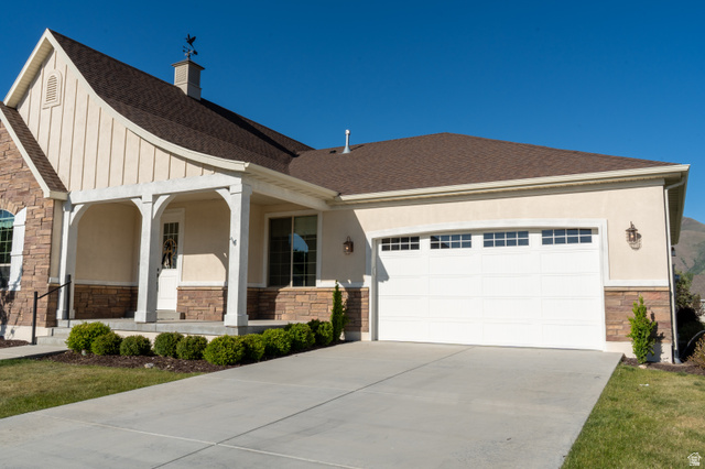 1222 West 190th Street North Mapleton, UT 84664 - Photo 44 of 46 Stone and stucco exterior featuring a covered porch entry, a two-car garage with transom windows, a concrete driveway, and a shingle roof with a cupola and weathervane
