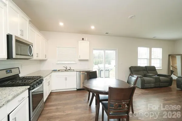 a kitchen with stainless steel appliances granite countertop a stove a sink a refrigerator a dining table and chairs